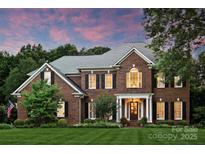 Elegant brick home showcasing manicured landscaping and a welcoming front porch, set against a colorful dusk sky at 159 Carsons Pl, Mooresville, NC 28117