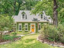Charming green home with dormer windows and a vibrant orange front door, set amidst lush landscaping and mature trees at 7639 Winterset Dr, Charlotte, NC 28270