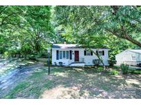 Charming single-story home with a brick foundation, black shutters, and a vibrant red front door nestled among mature trees at 828 Williams St, Gastonia, NC 28052