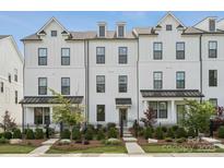 Charming exterior of a three-story white brick townhouse with manicured landscaping and a black iron fence at 4148 Alexander View Dr, Charlotte, NC 28226