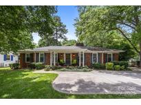 Charming brick home with a manicured lawn, concrete driveway, and a welcoming front porch with seating at 5640 Sharon Rd, Charlotte, NC 28210