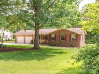 Charming single-story brick home with red shutters, attached two-car garage, mature trees, and a green lawn at 10728 Forest Dr, Matthews, NC 28105