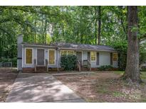 Charming single-story home with a gray facade, a concrete driveway, and mature trees in a wooded setting at 5143 Delivau Dr, Charlotte, NC 28215