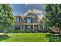 Brick two-story home with manicured lawn, lush trees and shrubbery under a blue sky with puffy white clouds at 3913 Widgeon Way, Waxhaw, NC 28173