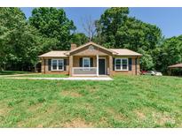 Charming brick home with a covered porch and front yard, surrounded by trees at 142 Single Oak Dr, Troutman, NC 28166