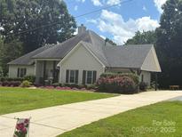Charming single-story home boasts a manicured lawn, blooming flowers, and a long driveway leading to a covered carport at 5701 Cedar Hill Dr, Monroe, NC 28110