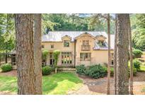 An attractive beige home with a metal roof, manicured lawn and stone pathway, framed by mature trees at 177 Yadkin Falls Rd, New London, NC 28127