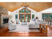 Bright living room featuring wood-paneled ceiling, fireplace, large windows, and access to the outdoor scenery at 6259 River Cabin Ln, Charlotte, NC 28278