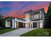Elegant, modern home with black framed windows, a balcony and black garage doors against a vibrant sunset sky at 3308 Carmel Rd, Charlotte, NC 28226
