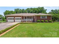 Charming brick home featuring an attached two-car garage and a welcoming front porch at 128 Howie St, Mount Holly, NC 28120