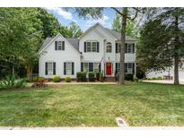 Charming two-story home with a well-manicured lawn, red front door, and mature landscaping, in a quiet neighborhood at 11624 Crossroads Pl, Concord, NC 28025