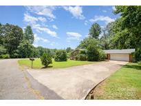 Ranch-style home featuring a well-manicured lawn, mature trees, and a large driveway leading to an attached garage at 165 Fieldstone Farm Dr, Statesville, NC 28625