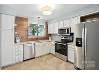 Bright kitchen featuring white cabinets, stainless steel appliances, and stylish wood accent wall at 3020 Heathstead Pl # A, Charlotte, NC 28210