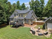 Expansive backyard featuring a deck, patio with a fire pit, and lush green lawn surrounded by mature trees at 3020 Waxhaw Crossing Dr, Waxhaw, NC 28173