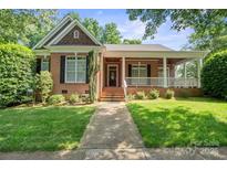 Charming brick home with a well-manicured lawn and inviting front porch, shaded by mature trees on a sunny day at 320 Magnolia St, Davidson, NC 28036