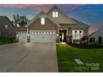 Inviting home with a two-car garage, stone accents, manicured lawn, and charming curb appeal at dusk at 17733 Burnt Hickory Dr, Charlotte, NC 28278