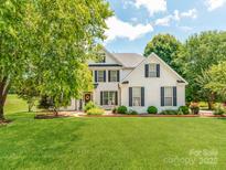 Charming white brick home featuring a lush green lawn, mature trees, and manicured landscaping at 1605 Ambergate Dr, Waxhaw, NC 28173
