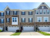 Charming townhouse exterior featuring stone accents, neutral siding, and attached garages under a clear blue sky at 411 Lahinch Dr, Tega Cay, SC 29708