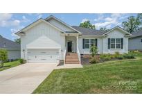 Charming home featuring a manicured lawn, brick stairs, and a two-car garage, set against a blue sky at 7739 Village Pkwy, Locust, NC 28097