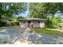 Quaint one-story home featuring light gray siding, a brick foundation, and a compact, gravel driveway at 1224 Hollywood Ter, Albemarle, NC 28001