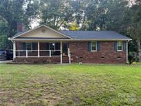 Charming single-story brick home with a cozy front porch and mature trees surrounding the property at 6039 Donna Dr, Charlotte, NC 28213