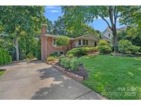 Charming brick home with lush landscaping, mature trees, and a long driveway on a sunny day at 5441 Wintercrest Ln, Charlotte, NC 28209