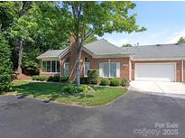 Brick home featuring a well-maintained front yard, attached garage, and a mature tree providing shade at 8465 Olde Troon Dr, Charlotte, NC 28277