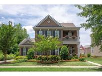 Charming two-story brick home featuring a double porch, lush landscaping, and an American flag at 10818 Alvarado Way, Charlotte, NC 28277