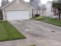 Tan single-story home with two-car garage and well-maintained landscaping at 569 River View Dr, Lowell, NC 28098