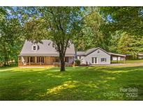 Charming home featuring a covered porch, metal roof, light siding, and lush landscaping at 265 River Run Rd, Statesville, NC 28625