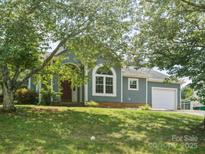 Charming home with a blue exterior, arched window, attached garage, and well-maintained lawn and mature trees at 8323 Bedford Green Ln, Charlotte, NC 28215