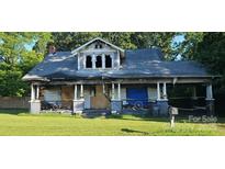 Overgrown property with a rundown two-story home featuring a covered porch and visible damage at 619 N Main St, Landis, NC 28088