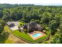 Stunning aerial view of a brick home with a pool and detached garage surrounded by lush greenery at 929 Blacksnake Rd, Stanley, NC 28164