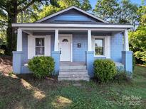 Charming light blue home featuring a cozy front porch with white columns and trimmed windows with a landscaped yard at 116 Honeywood Ave, Charlotte, NC 28216