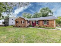 Charming brick home featuring a well-manicured lawn, colorful landscaping, and complementary colored shutters and front door at 6421 Hidden Forest Dr, Charlotte, NC 28213
