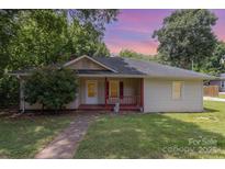Charming single-story home with a cozy front porch and mature trees against a colorful sunset sky at 210 Tuckaseege Rd, Mount Holly, NC 28120