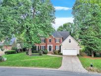 Brick home with an attached garage, green lawn, and mature trees providing lots of shade at 5015 Foxbriar Trl, Charlotte, NC 28269