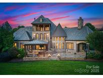 Expansive rear exterior showcasing a sprawling brick home with an outdoor kitchen and stone patio at twilight at 300 Eagle Bend Dr, Waxhaw, NC 28173