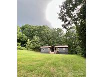 Charming single-story home with a dark exterior, red metal roof, wooden porch and well-maintained lawn surrounded by lush trees at 6581 Emerald Isle Dr, Sherrills Ford, NC 28673