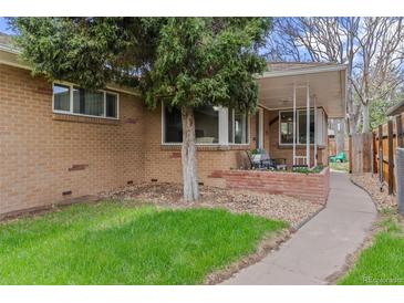 Charming brick home with a lush green lawn, mature tree, and covered porch area with seating at 3667 Hudson St, Denver, CO 80207
