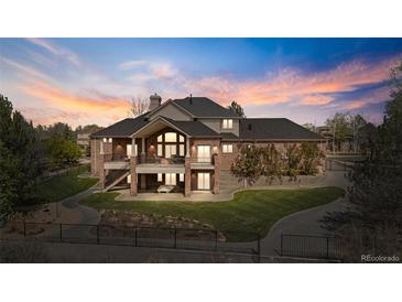 Expansive brick home with a deck, lush lawn, mature trees, and a driveway winding through a gated entrance at 3 White Pelican Cir, Thornton, CO 80241