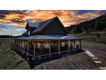 Charming two-story home with a wrap-around porch, set against a stunning sunset sky, offers picturesque outdoor living at 8191 S Homesteader Dr, Morrison, CO 80465