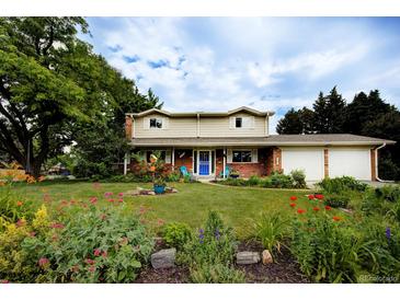 Charming two-story home with a well-manicured lawn, beautiful flowerbeds and a bright blue front door at 10373 W 75Th Ave, Arvada, CO 80005