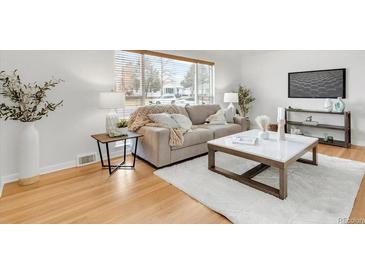 Bright living room featuring a neutral couch, white rug, light-colored hardwood floors, and natural light at 479 S Kendall St, Lakewood, CO 80226