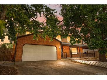 Two-story brick home featuring an attached two-car garage and covered front porch under a colorful evening sky at 1758 S Tucson St, Aurora, CO 80012