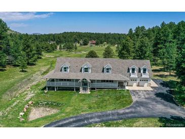 Expansive home with a large wraparound porch, manicured lawn, and an attached two-car garage at 3619 Estates Cir, Larkspur, CO 80118
