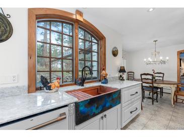 Bright kitchen with a copper sink, white marble countertops, white cabinetry, and a view of the outdoors at 689 Red Deer Rd, Franktown, CO 80116