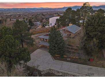 An aerial view shows a home surrounded by trees and a driveway leading to the garage with mountain views in the distance at 8258 W 66Th Dr, Arvada, CO 80004