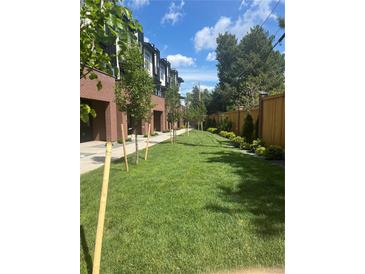 Brick townhomes showcase a manicured lawn and freshly planted trees under a bright, partly cloudy sky at 2144 Applewood Dr, Lakewood, CO 80215