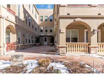 Exterior of a tan home with brick courtyard, covered entrances and manicured landscaping at 40 Madison St # 103, Denver, CO 80206